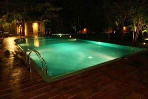 A swimming pool at night with a wooden deck and a small building in the background. - Nil diya mankada safari lodge (Udawalawa)