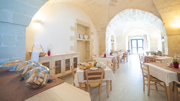 Un vaste espace de salle à manger doté de hauts plafonds en arc et de murs en pierre, comprenant plusieurs tables et chaises, et un espace central ouvert menant à une porte.