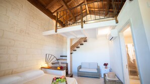 Une chambre avec un espace en mezzanine, un lit agrémenté d’un plateau de fruits, un fauteuil en osier et un escalier menant à un balcon.
