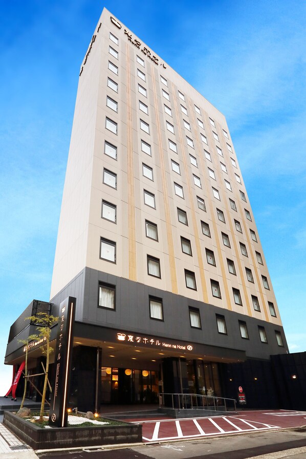 Un grand immeuble d’hôtel au design moderne, avec une entrée imposante dotée d’une façade en verre et d’une enseigne indiquant qu’il s’agit de l’hôtel Hennna.