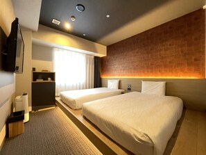 Une chambre d’hôtel avec deux lits, un téléviseur à écran plat, un bureau avec une chaise et une fenêtre avec des rideaux.