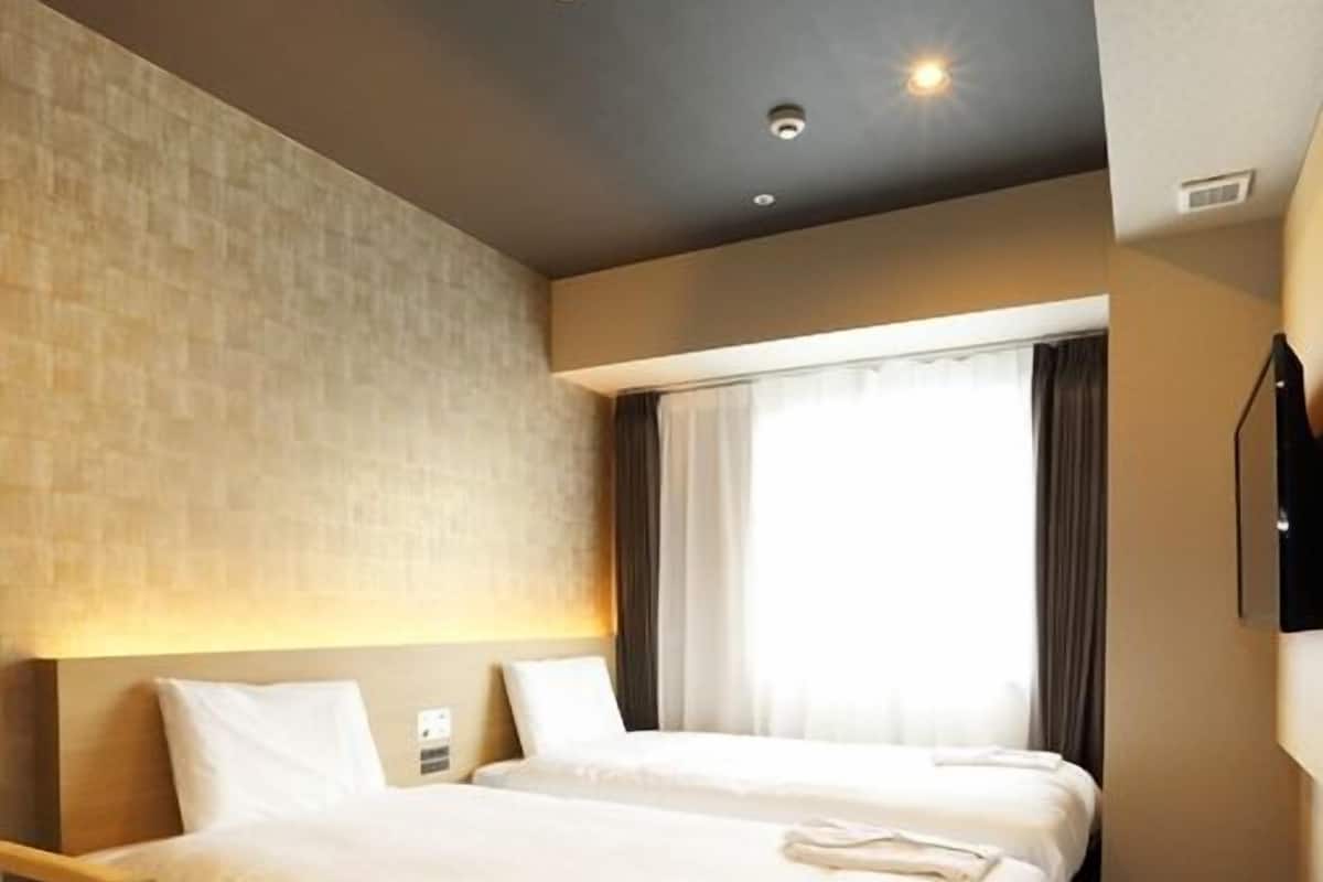 Une chambre d’hôtel avec un grand lit, une table de chevet, un téléviseur à écran plat fixé au mur et une fenêtre avec des rideaux.