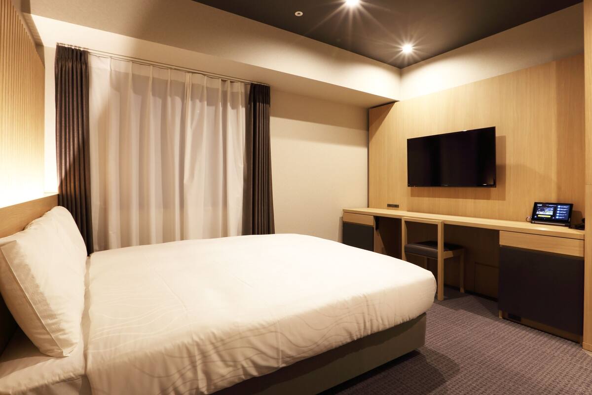 Une chambre d’hôtel équipée d’un lit, d’un bureau, d’un téléviseur à écran plat et d’un panneau de commande.