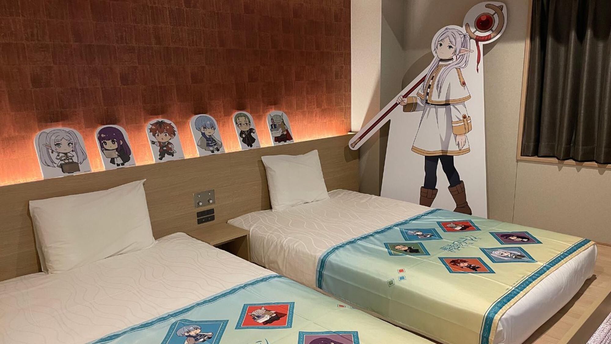 Een hotelkamer met twee bedden, een bakstenen muur, posters van anime personages en een groot kartonnen uitsnede van een anime personage aan de muur.