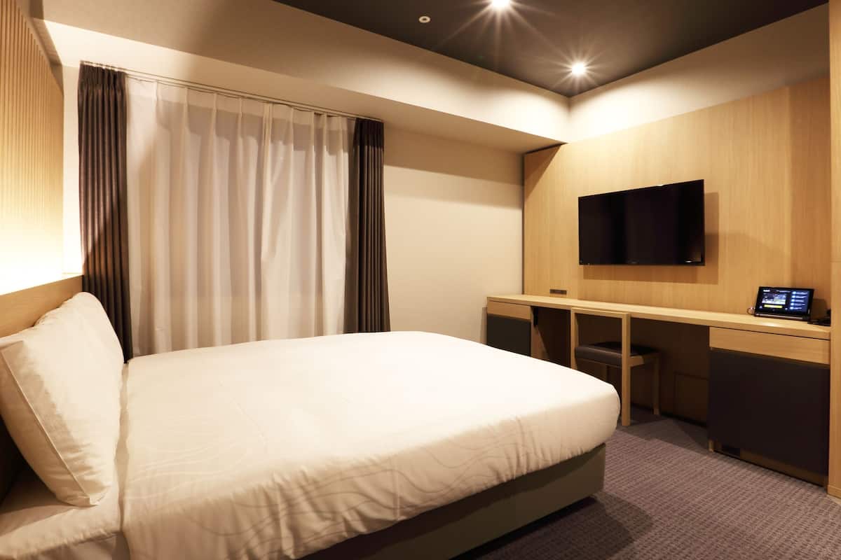 Une chambre d’hôtel équipée d’un lit, d’un bureau, d’une télévision et d’un panneau de commande.