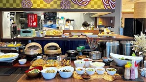 A buffet setup with various food items and a staff member in the background.