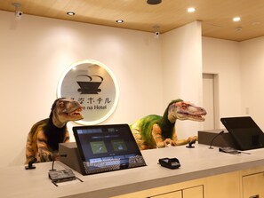 A reception desk with a digital display, a sign with a dinosaur illustration, and a camera on the ceiling. - Henn na Hotel Kanazawa Korinbo (Kanazawa)
