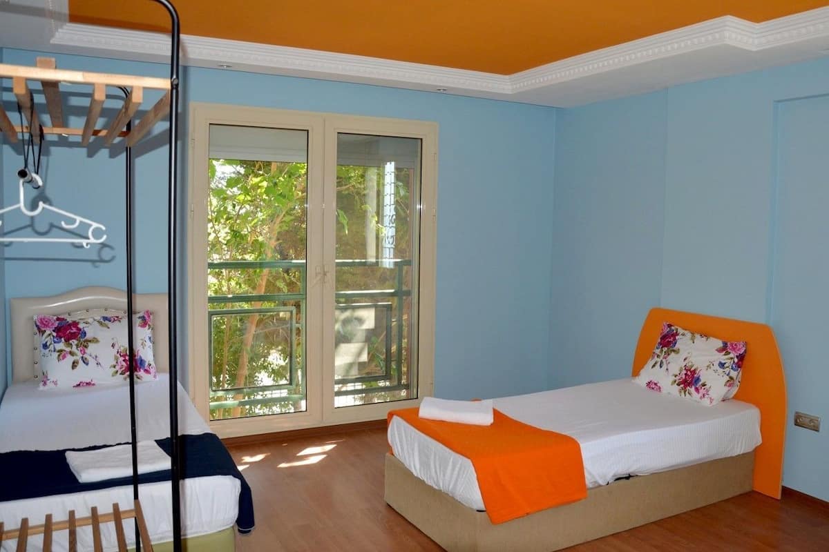 A bedroom with two beds, a wooden floor, and a large window with a view of trees.