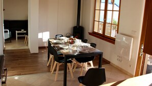 Un comedor con una mesa de madera dispuesta para cuatro, una estufa negra y un ventanal con vistas al exterior.