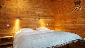Una habitación de cabaña de madera con una cama, dos luces fijadas a la pared y un perchero.
