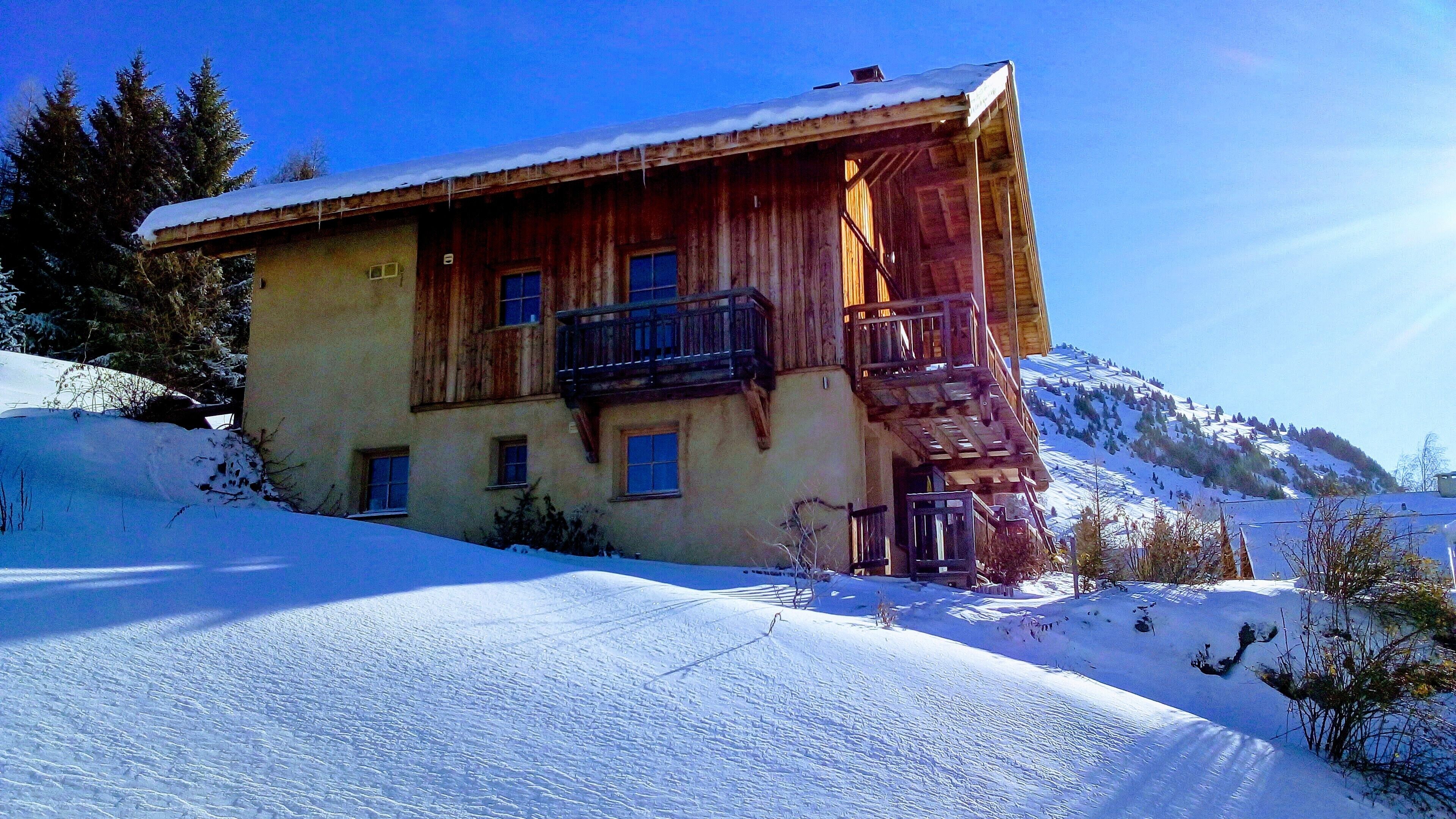 A wooden chalet with a balcony, surrounded by snow-covered hills.