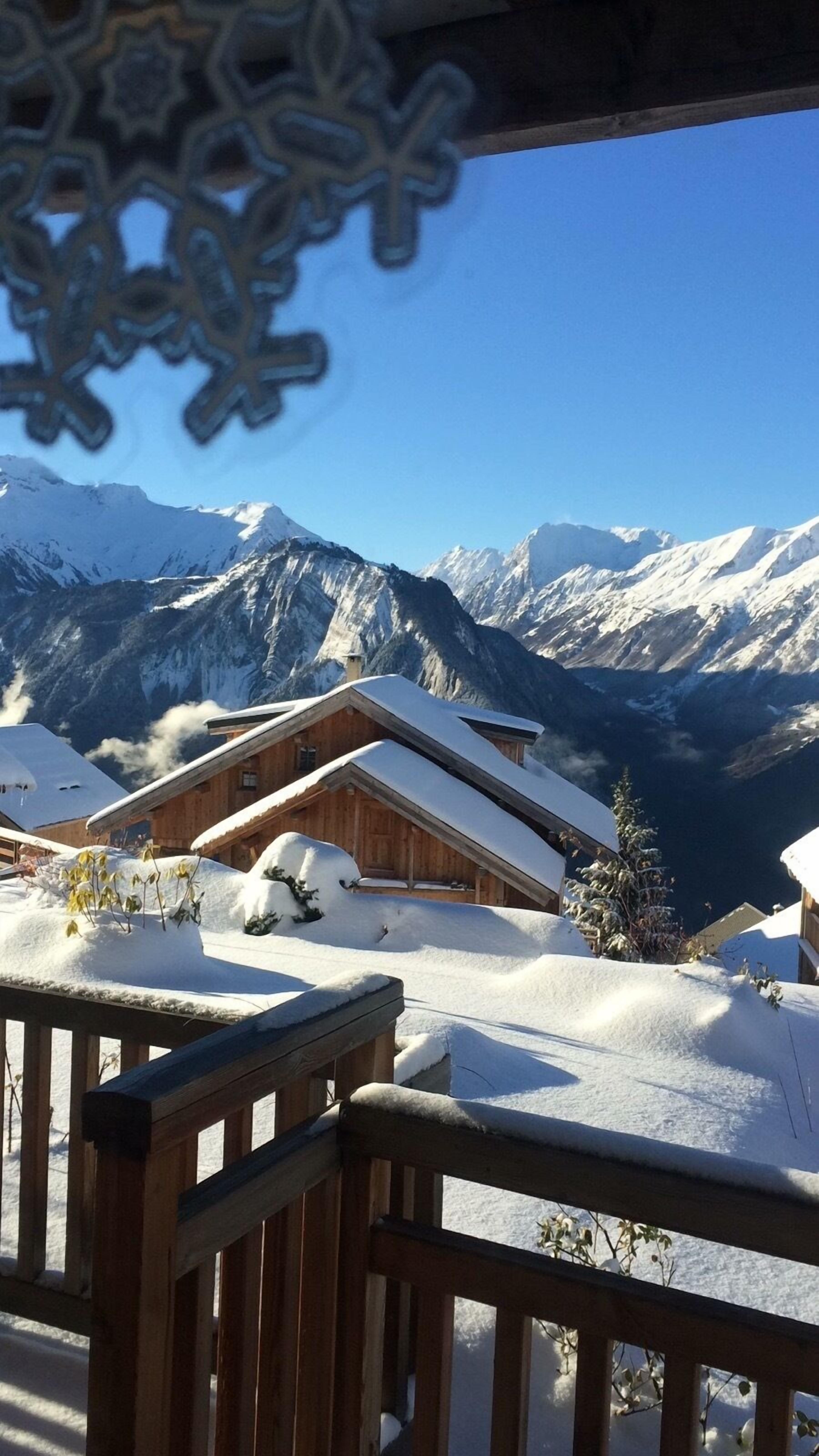 Un chalet in legno con tetto imbiancato dalla neve, sullo sfondo di montagne innevate sotto un cielo azzurro.