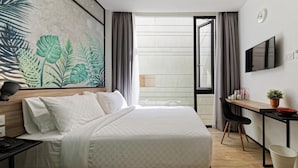 A hotel room with a bed, a desk, a chair, a TV, and a large window with curtains. - Daun Residence Bandung (Bandung)