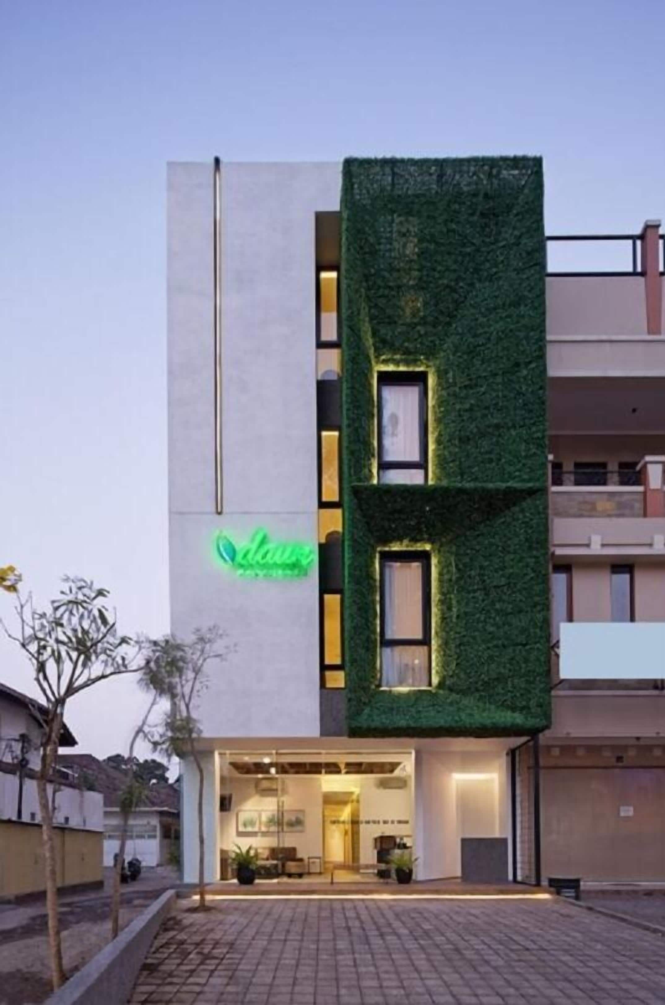 Edifici modern amb un jardí vertical verd a la façana, un signe de neó i una entrada ben il·luminada.