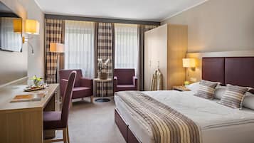 Quarto de hotel com uma cama, duas poltronas, uma escrivaninha e uma mesinha.