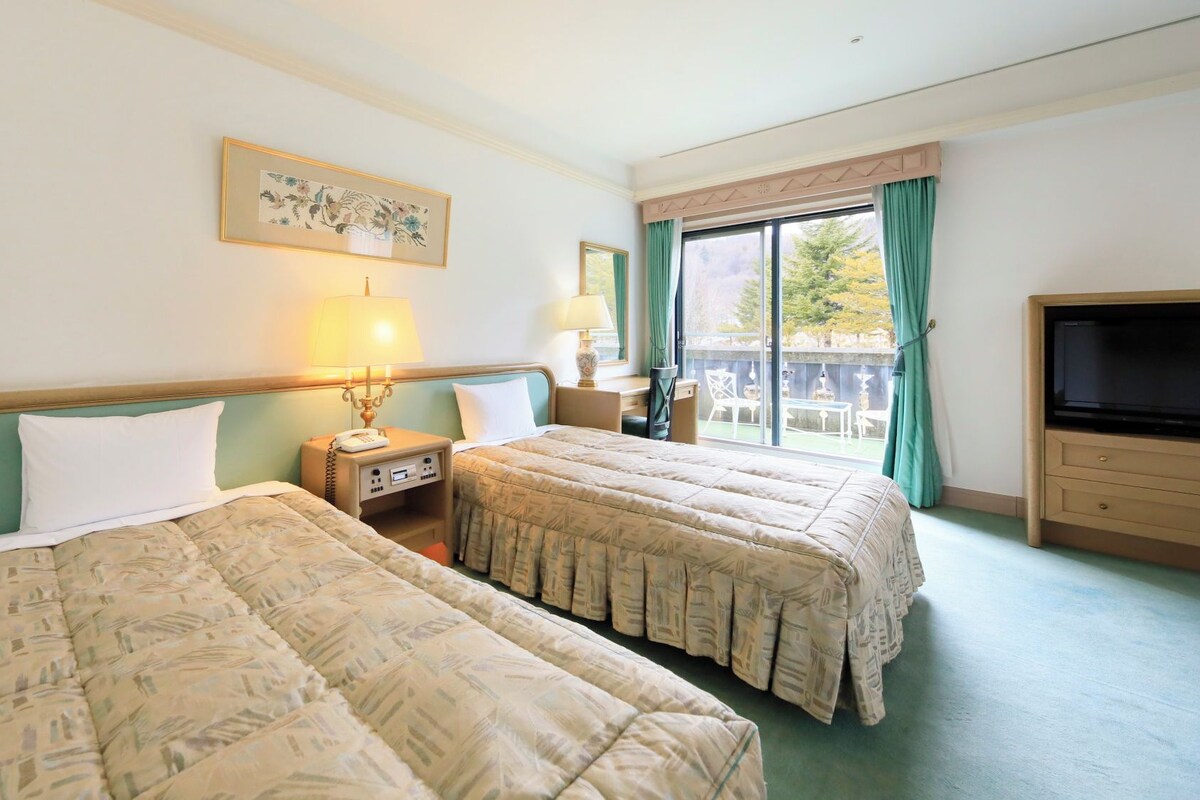Une chambre d’hôtel avec deux lits, une télévision, un bureau et un balcon avec vue.