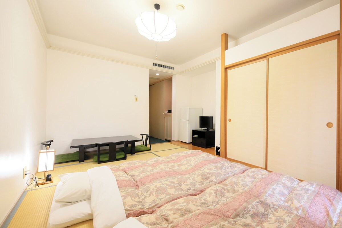 A hotel room with a bed, a desk, a chair, a television, and a wardrobe.