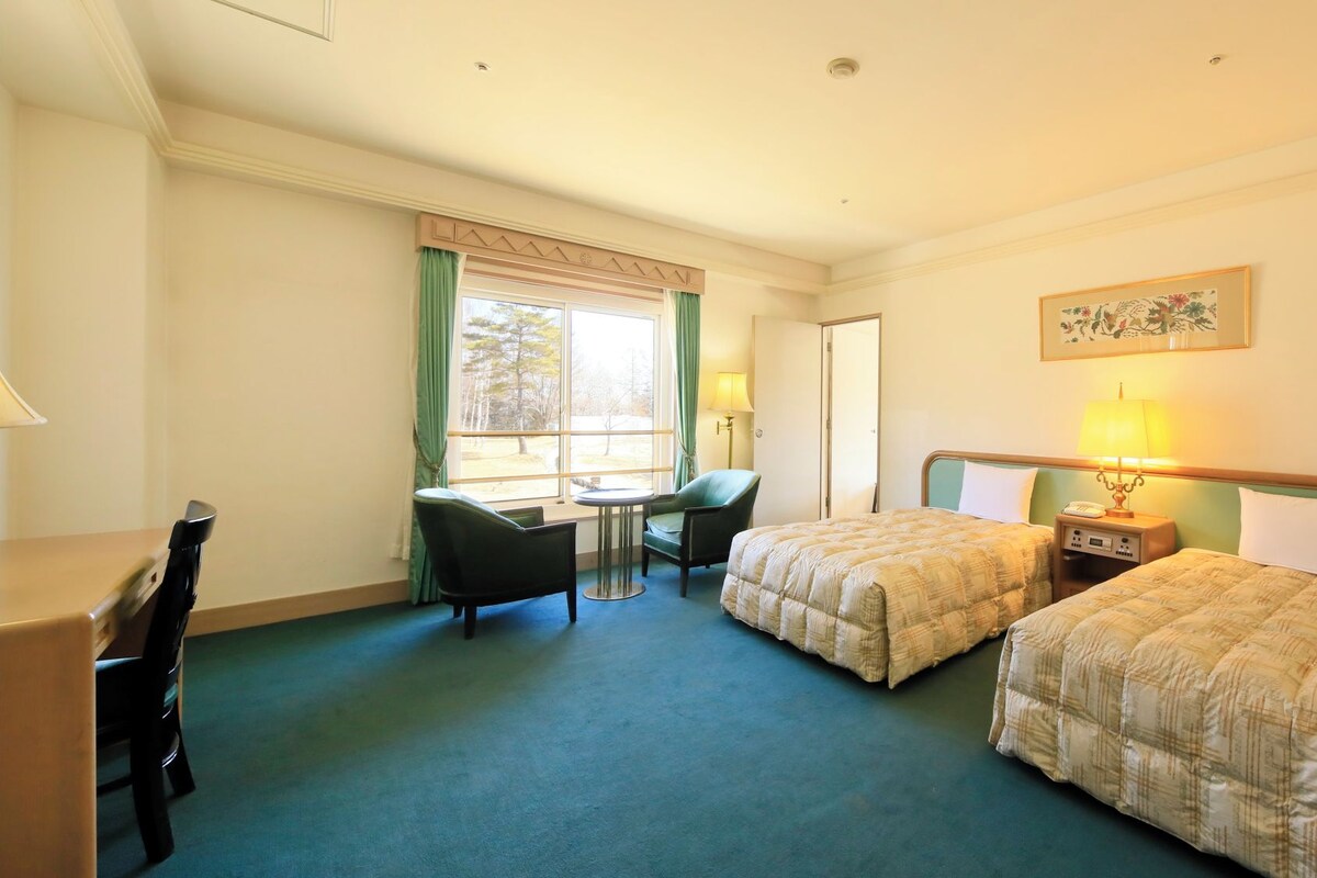 A hotel room with two beds, a desk, a chair, and a window with curtains.