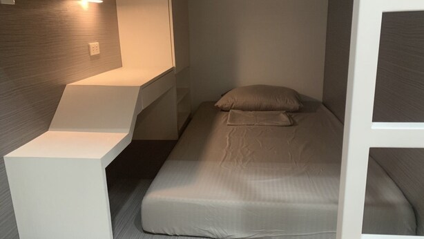 A compact room with a bed, a desk, and a wall-mounted light. - OTravel Hostel (Lapu-Lapu)