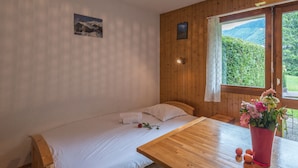 A wooden cabin room with a bed, a table, a window with a view of greenery, and a hanging light fixture. - Cozy studio in Chamonix - Pets allowed, private parking (Chamonix-Mont-Blanc)
