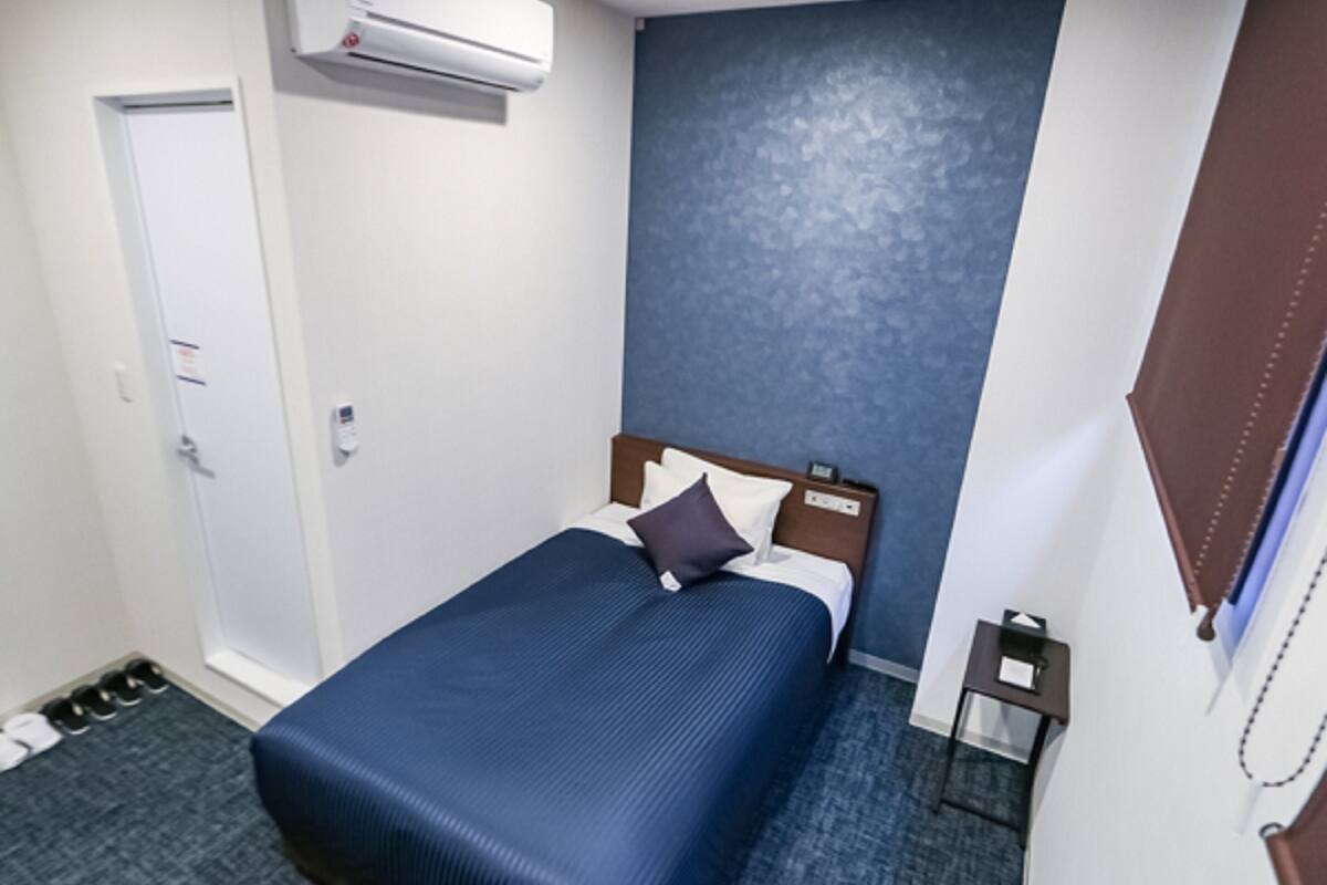 Quarto de hotel com cama, mesa de cabeceira, ar condicionado, porta e sapateira.