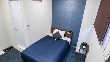 A hotel room with a bed, a nightstand, an air conditioning unit, a door, and a shoe rack.
