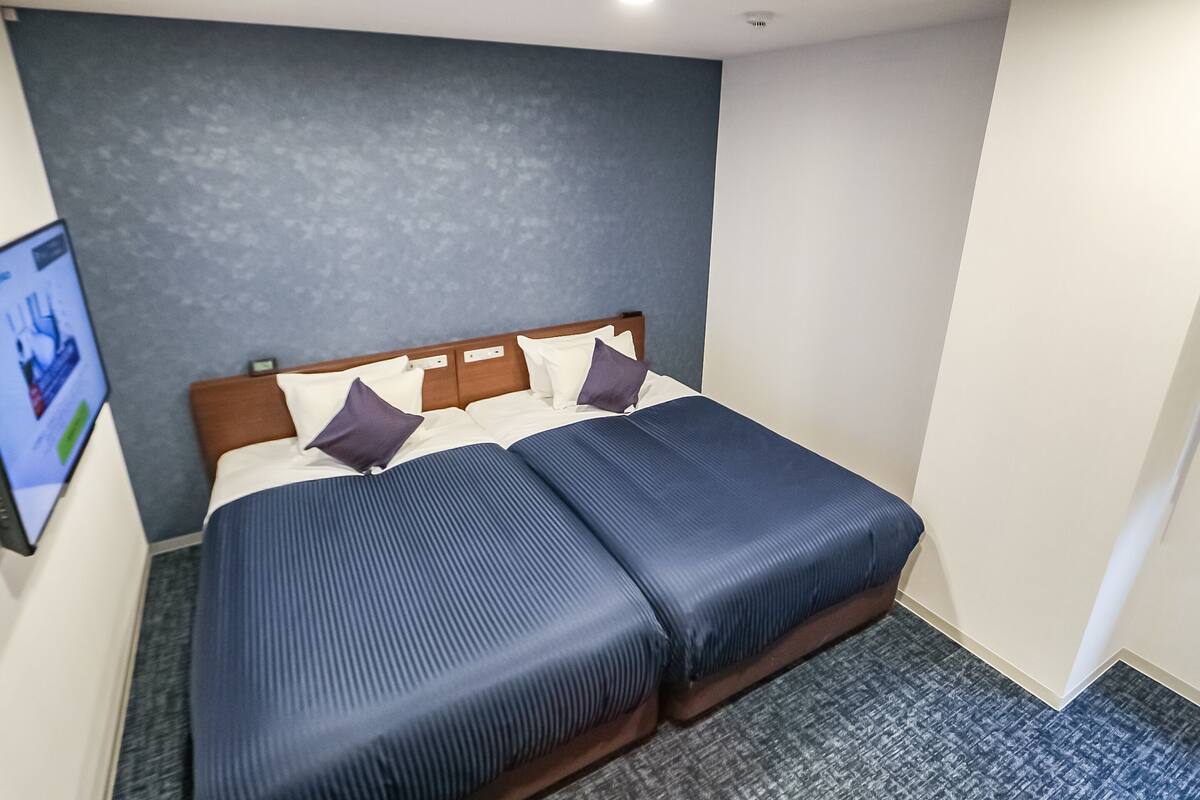 Quarto de hotel com uma cama, televisão na parede e carpete cinzento.