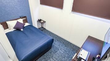 Een hotelkamer met een bed, een klein tafeltje, een televisie en een raam met jaloezieën.