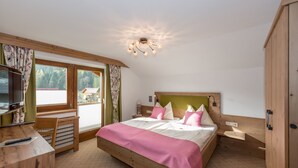 A bedroom with a wooden bed, a television, a desk, and a window with curtains. - Alpenecho (Ramsau am Dachstein)