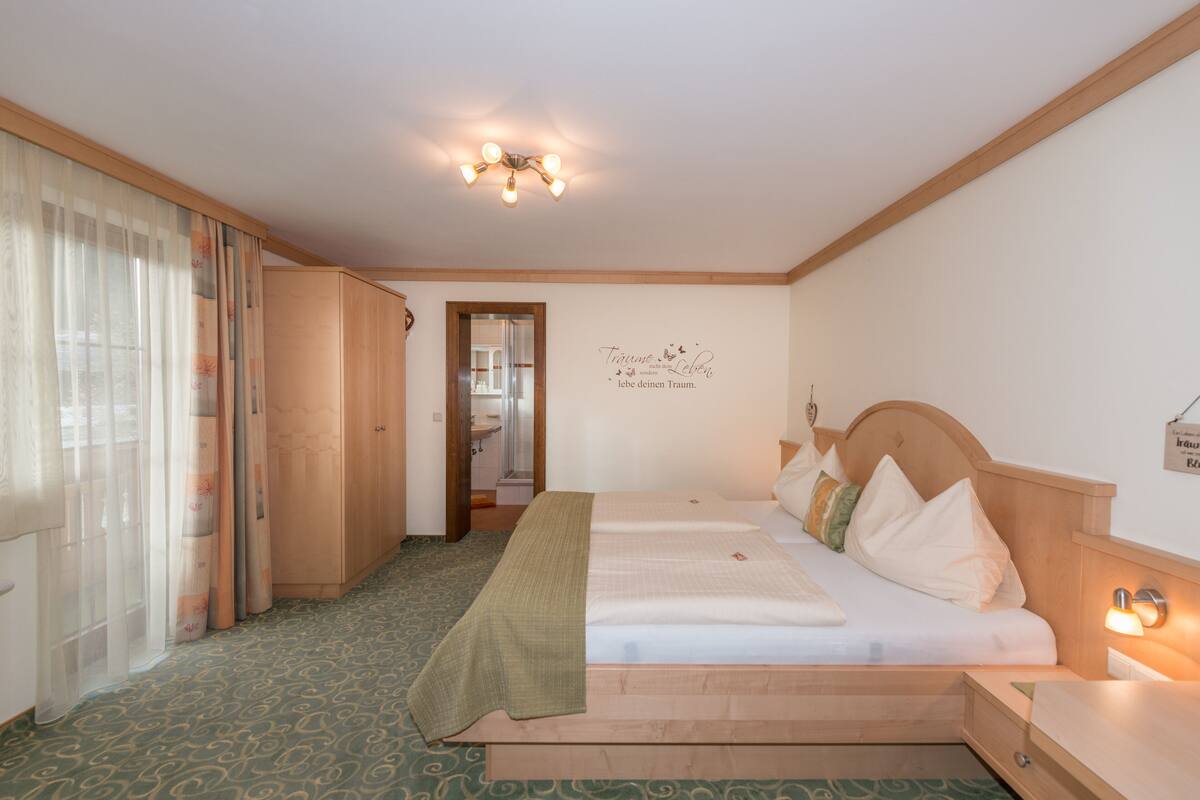 A hotel room with a bed, a bedside table, a mirror, a wardrobe, and a bathroom visible through an open door.