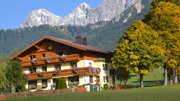 A traditional chalet with balconies adorned with flowers, set against a backdrop of snow-capped mountains. - Alpenecho (Ramsau am Dachstein)