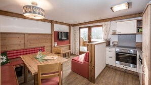 A compact kitchen with wooden cabinetry, a built-in oven, and a dining area with a bench and table. - Alpenecho (Ramsau am Dachstein)