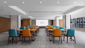 A conference room with rows of tables and chairs, a large projection screen, and a modern ceiling design.