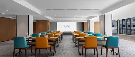A conference room with rows of tables and chairs, a large projection screen, and a modern ceiling design.