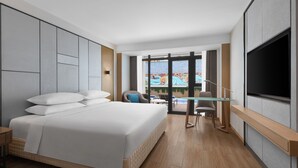 Habitación de hotel moderna con una cama grande, un televisor de pantalla plana, una mesa de vidrio y vistas a una piscina y zona exterior.