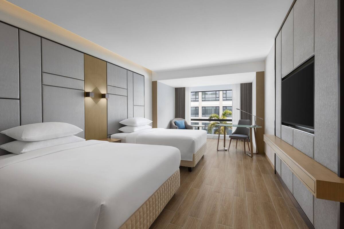 Una habitación de hotel moderna con dos camas, un escritorio y un televisor.