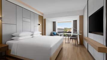 A modern hotel room with a large bed, a desk with a chair, a TV, and a balcony with a view.
