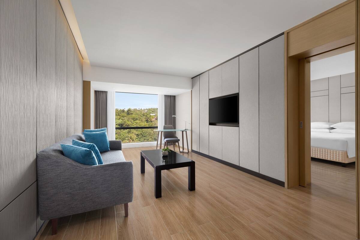 Una habitación de hotel moderna con sofá, una mesita, televisor y cama.