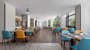 Un restaurante espacioso con techos altos, ventanas amplias y una larga zona de comedor con sillas azules y amarillas.