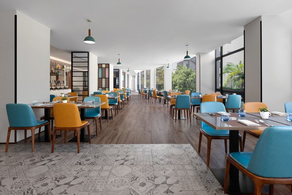 Un restaurante espacioso con techos altos, ventanas amplias y una larga zona de comedor con sillas azules y amarillas.