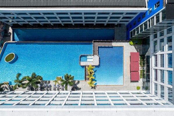 Una piscina en la azotea con vistas despejadas del cielo, rodeada de edificios modernos y palmeras.