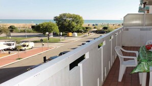 Een balkon met uitzicht op zee, een parkeerplaats en een tafel met stoelen.