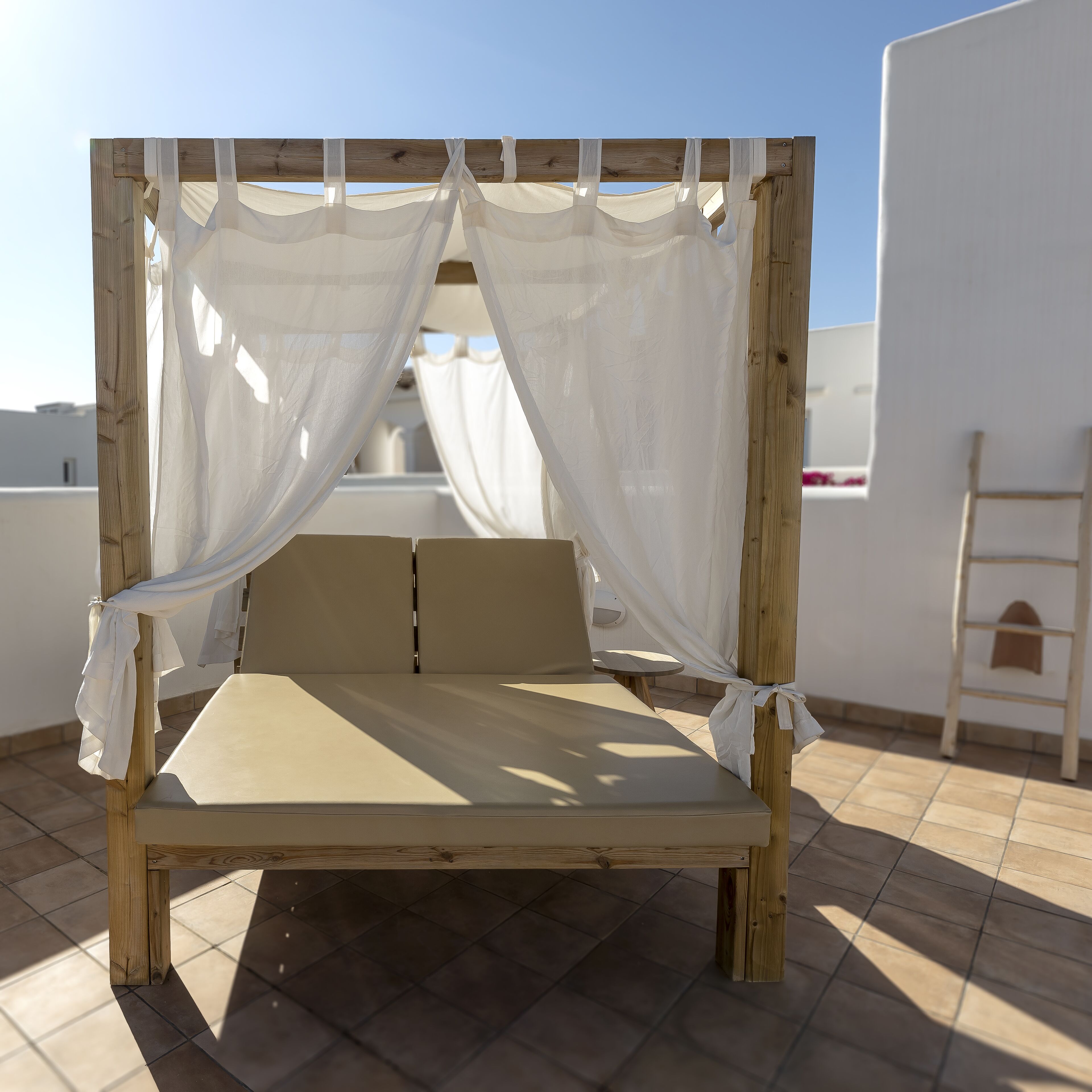 A wooden bed with white curtains, a tiled floor, and a view of the sky.
