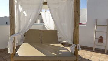 A wooden bed with white curtains, a tiled floor, and a view of the sky.