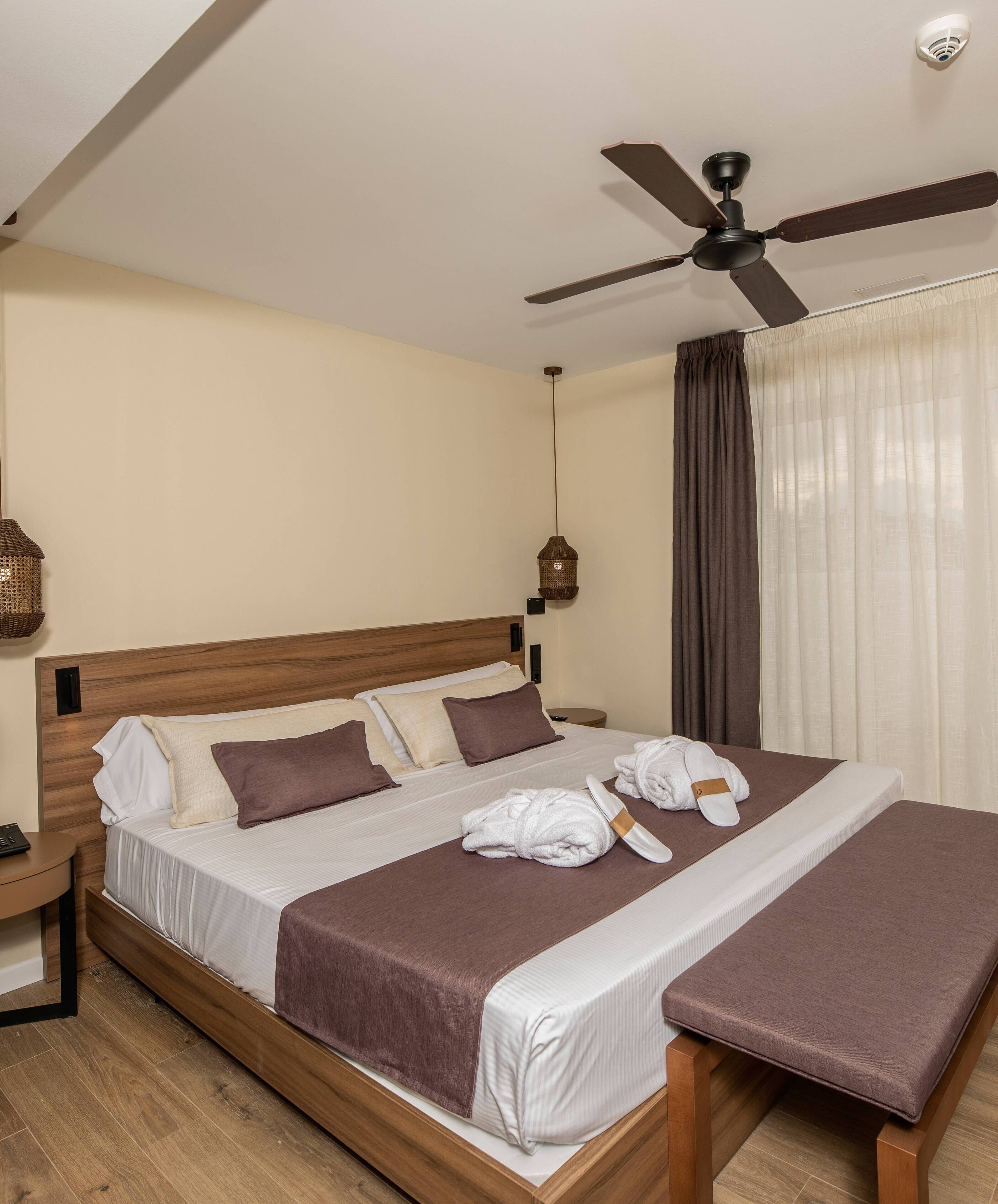 Una habitación de hotel con cama, mesita de noche, ventilador de techo e iluminación colgante.