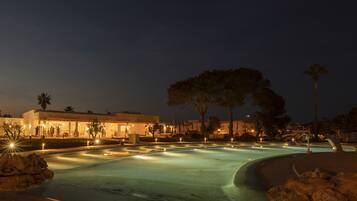 Vue nocturne d’un espace piscine avec un bâtiment en arrière-plan.