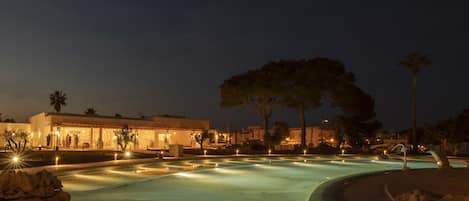 A nighttime view of a swimming pool area with a building in the background.