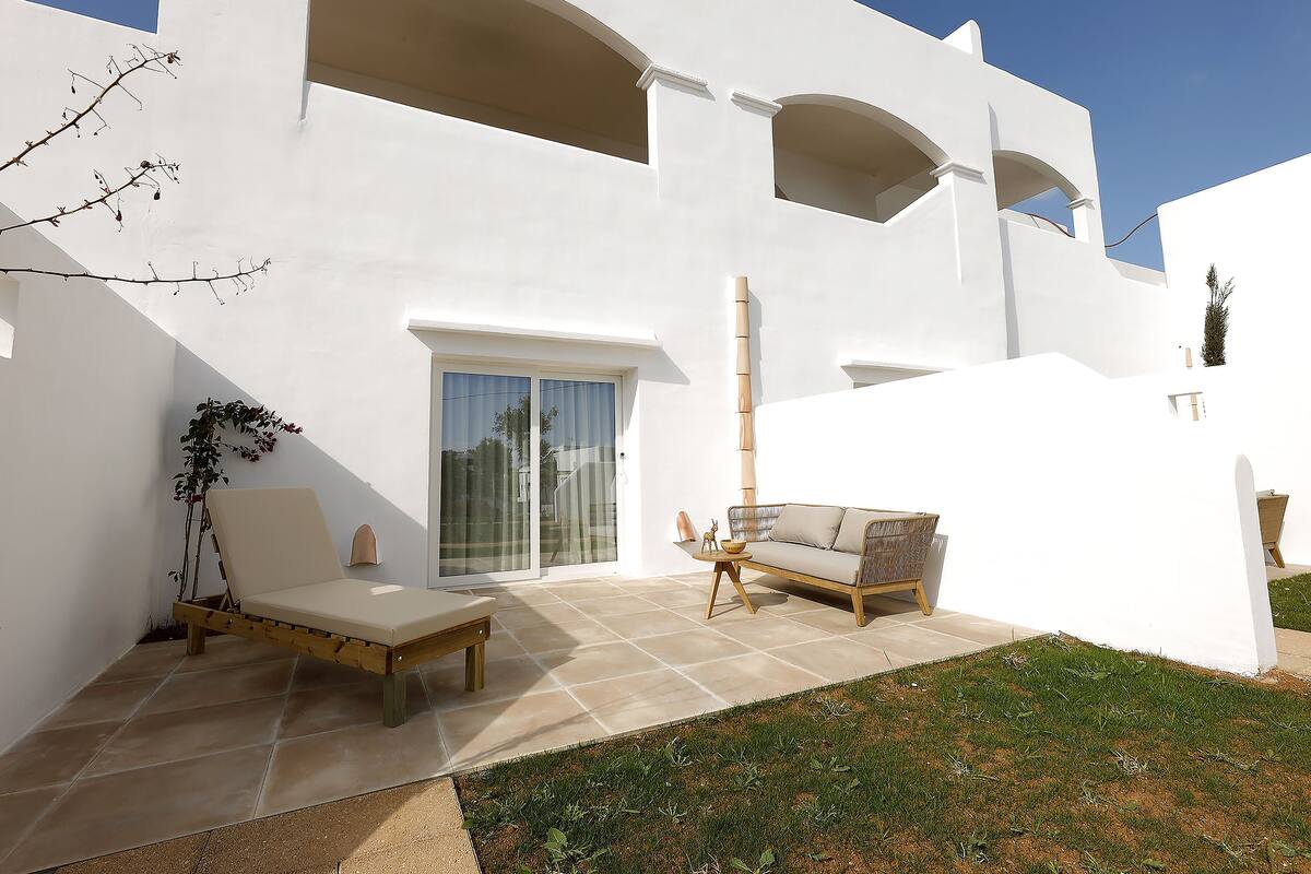 A modern white building with a patio area featuring a sofa, a wooden bench, and a small table.
