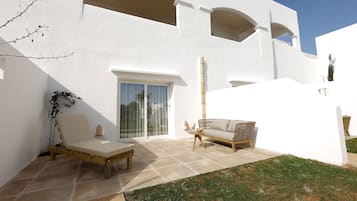 Un edificio moderno y blanco con un patio que incluye un sofá, un banco de madera y una pequeña mesa.