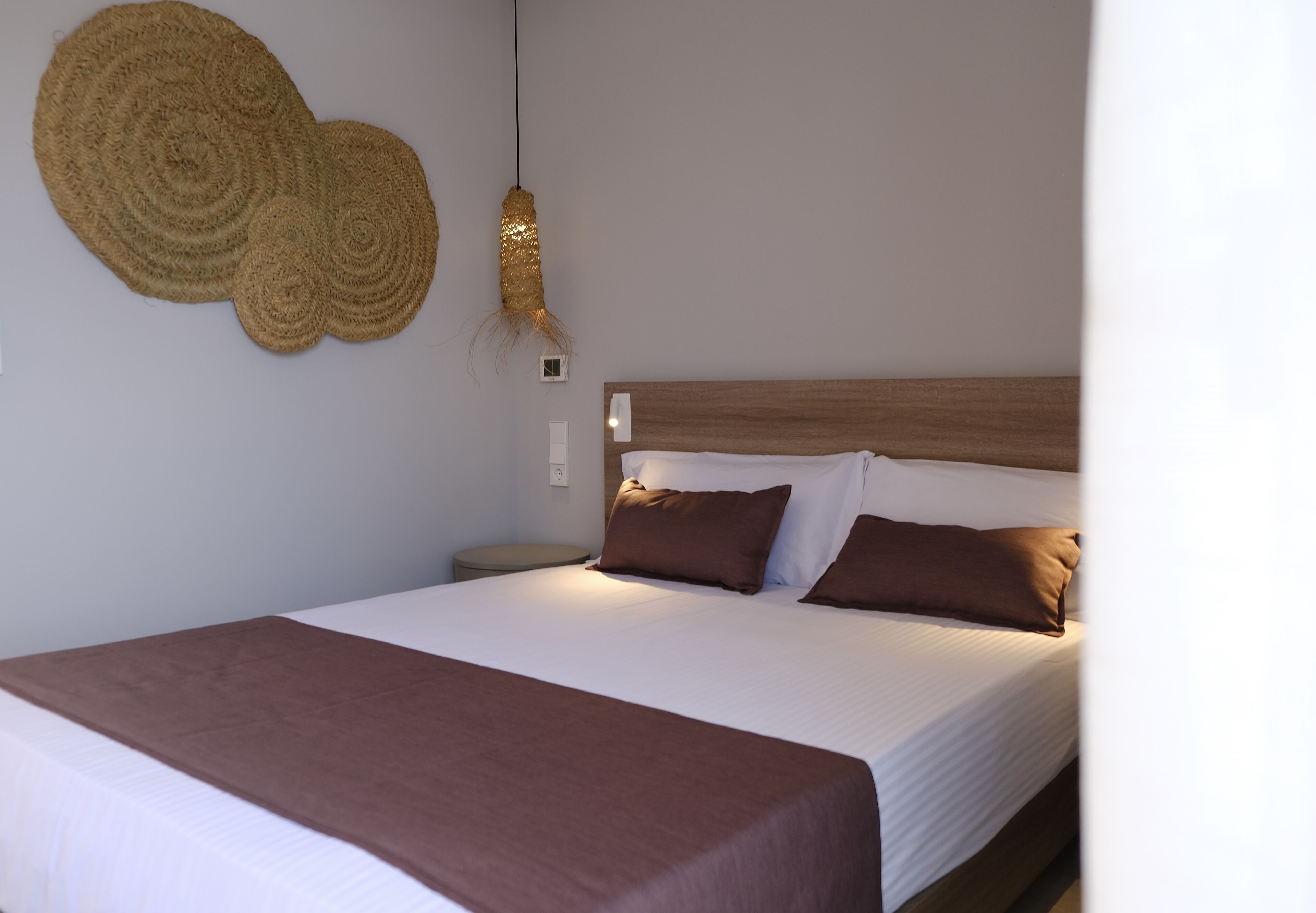 A neatly made bed with a brown bedspread and pillows, a wooden headboard, and a wall-mounted decorative item.